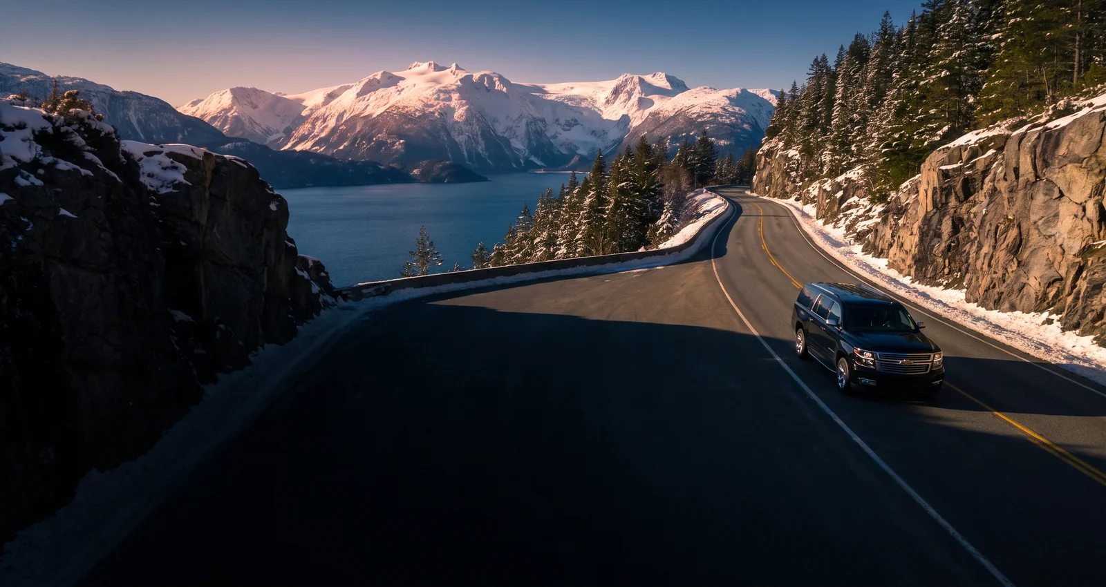 Black Chevrolet Suburban on a coastal mountain highway in winter