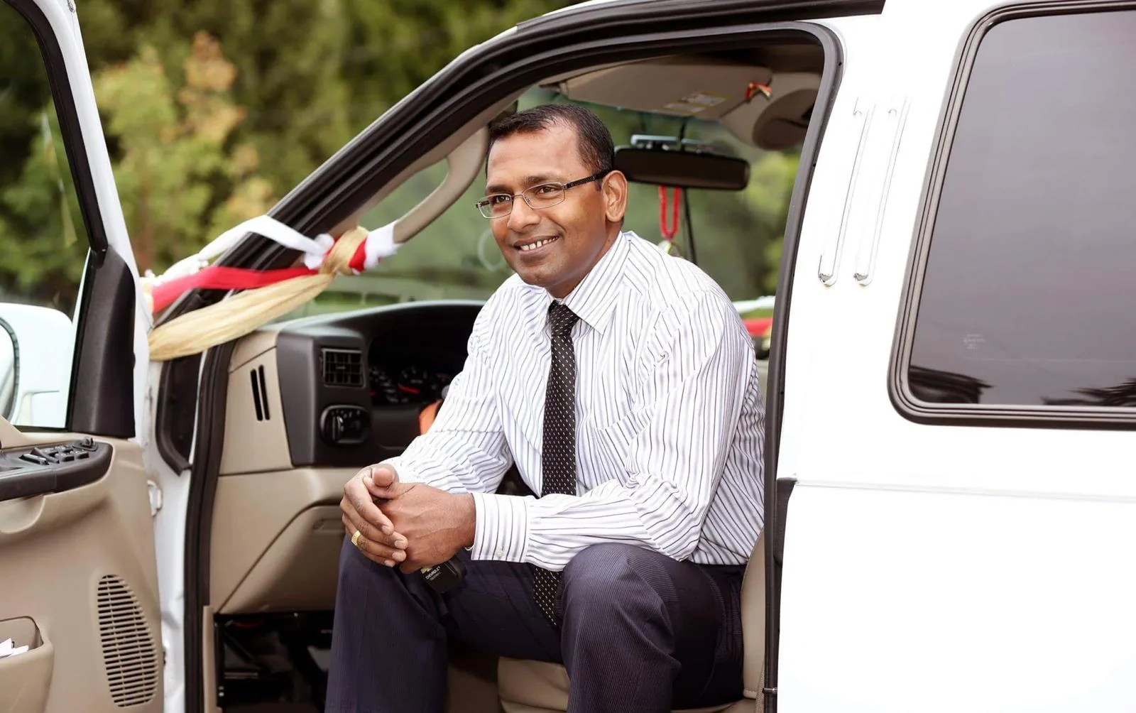 Jay, smiling, seated in the open door of a white limousine decorated with ribbons